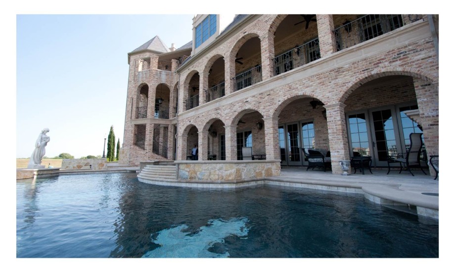 A mansion with a pool in front of it.