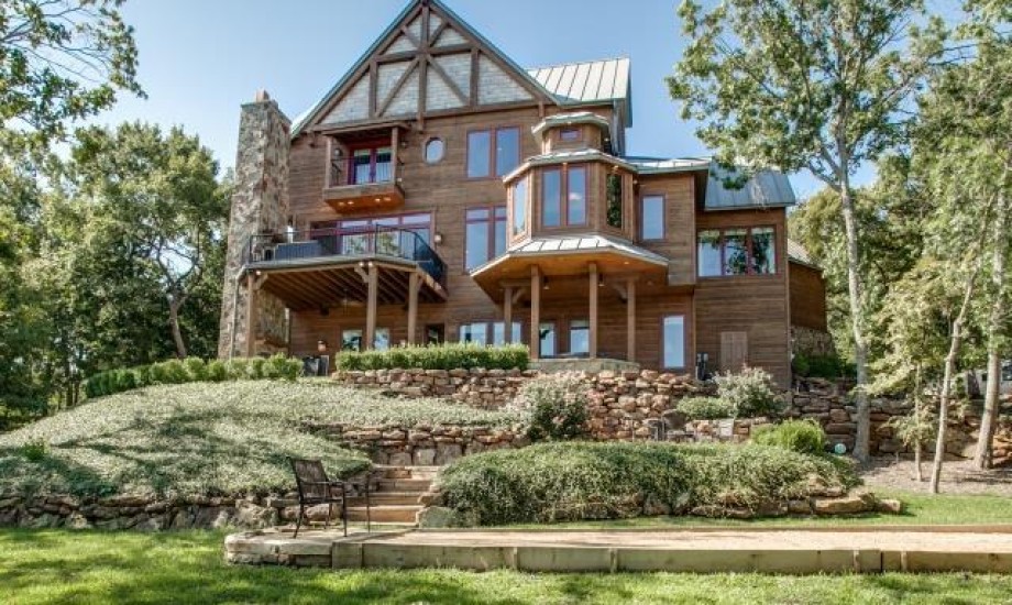 A large home with a large deck in the middle of a wooded area.